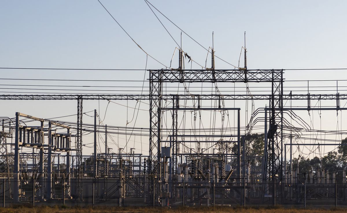 High voltage electrical substation with transmission gantries and power lines at an energy facility