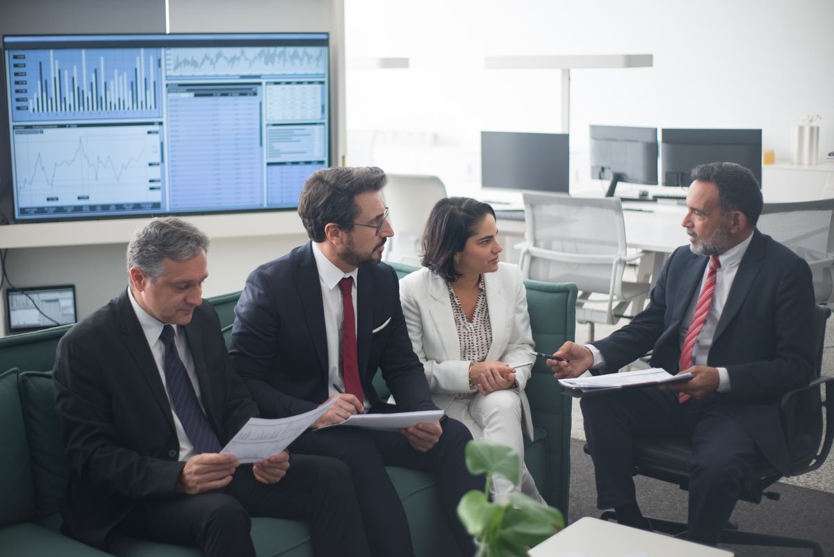 Bank operations team reviewing transaction volumes and channel availability against a wall display of financial charts